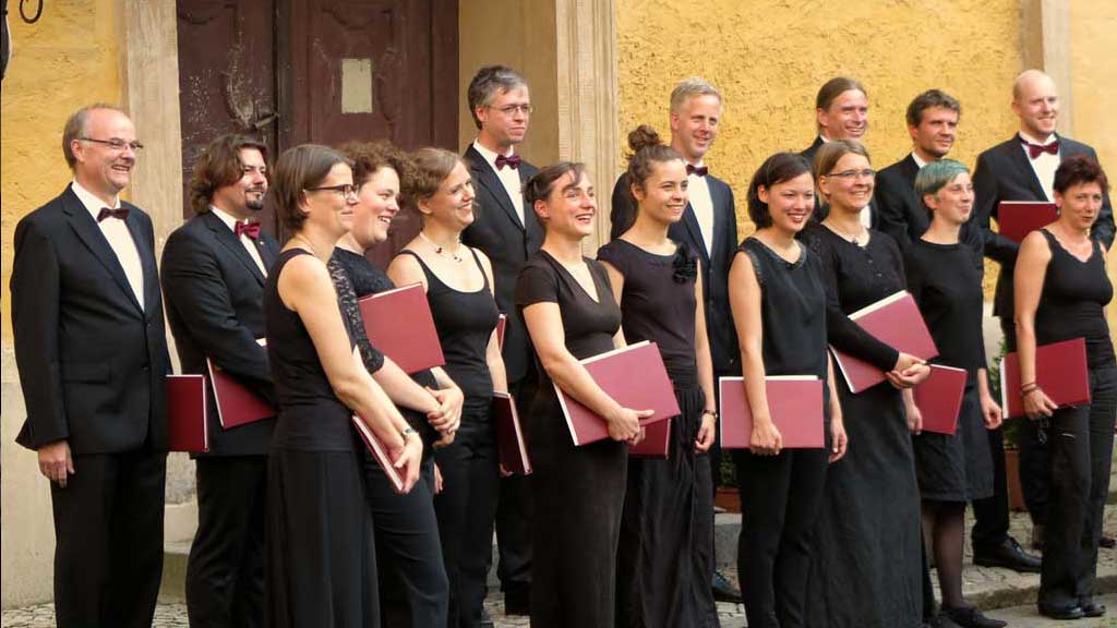 Sänger*innen des Kammerchor TASK stehen in Konzertkleidung vor einer Kirche.
